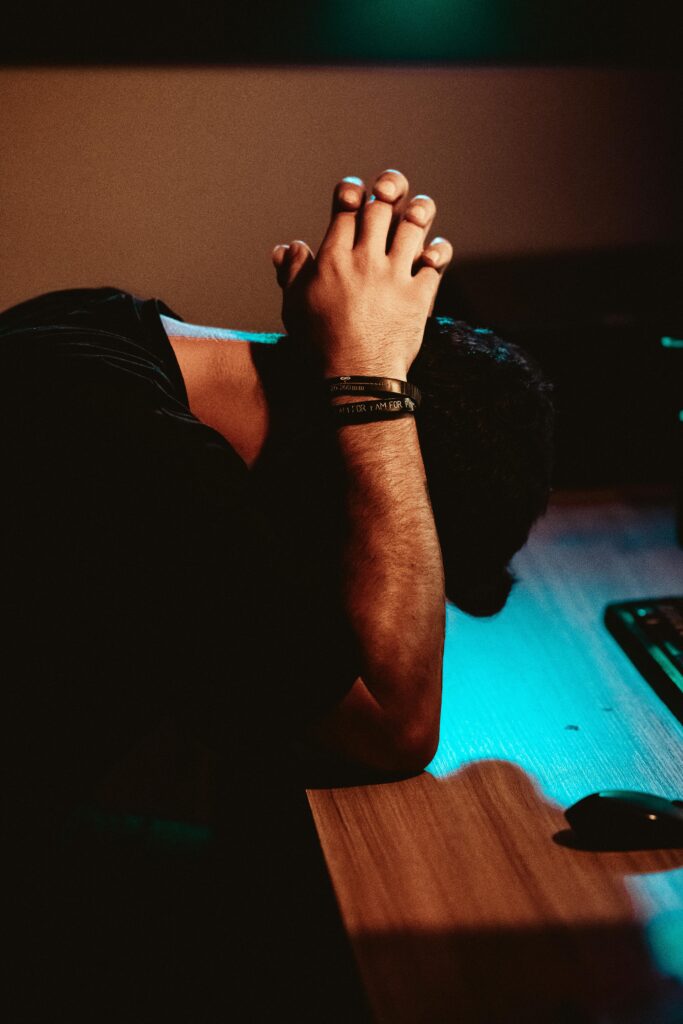 Man showing stress and exhaustion, leaning on a desk under dim lighting.
